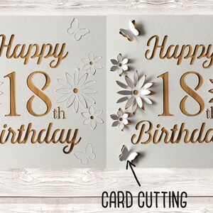May include: A white card with the words "Happy 18th Birthday" cut out in a wood-like pattern. The card is decorated with white paper flowers and butterflies.