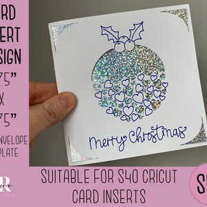 May include: A white card with a silver glitter design of a Christmas ornament with the text "Merry Christmas" in blue ink. The card measures 4.75 inches by 4.75 inches. The card is suitable for use with a Cricut S40.