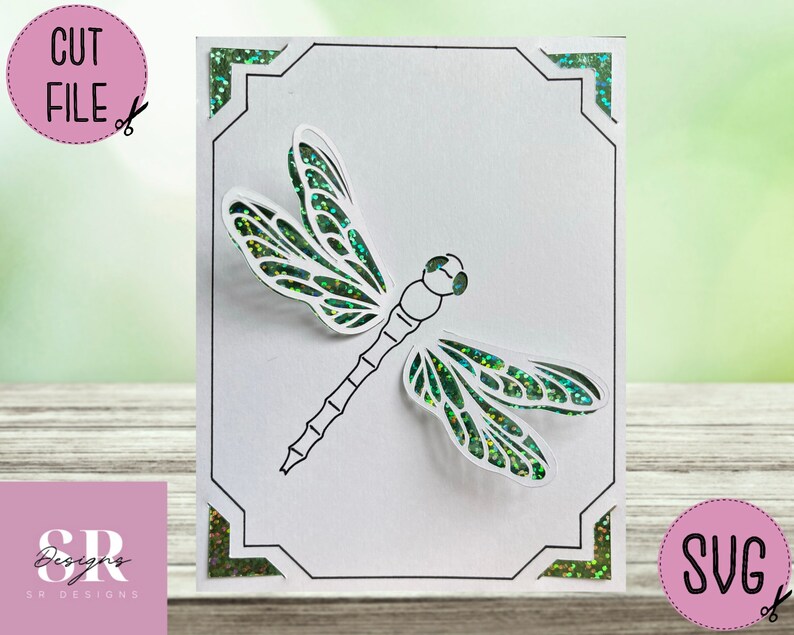 May include: A white card with a green glitter border and a black and white outline of a dragonfly with green glitter wings. The card has the text "SVG" in the bottom right corner.