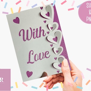 Pu&ograve; includere: Un biglietto bianco con le parole "With Love" in glitter viola. Il biglietto ha un bordo decorativo di cuori di carta sovrapposti.