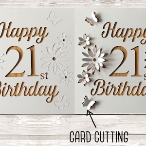 May include: A white card with the words "Happy 21st Birthday" cut out in a wood-like pattern. The card is decorated with white paper flowers and butterflies.