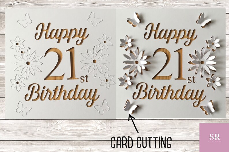 May include: A white card with the words "Happy 21st Birthday" cut out in a wood-like pattern. The card is decorated with white paper flowers and butterflies.