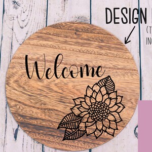 May include: A round wooden sign with the word "Welcome" in black cursive lettering and a black floral design in the lower right corner.