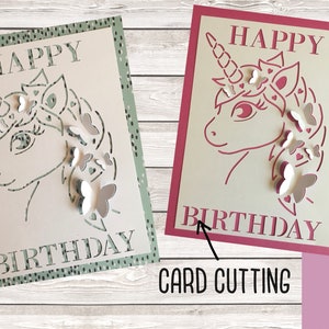 May include: Two birthday cards with a unicorn design. The card on the left is green with white butterflies and the card on the right is pink with white butterflies.