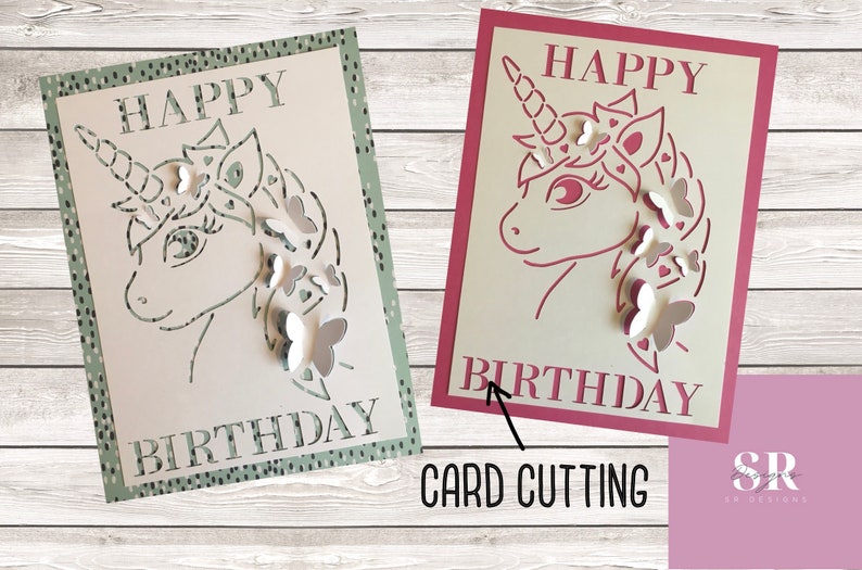 May include: Two birthday cards with a unicorn design. The card on the left is green with white butterflies and the card on the right is pink with white butterflies.