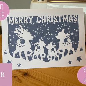 May include: A white card with a blue background and a white silhouette of a family of deer with the text "Merry Christmas" at the top.