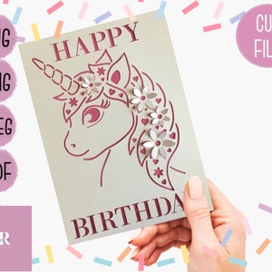 May include: A pink and white unicorn birthday card with the words "Happy Birthday" on the front. The unicorn has a flower crown and a pink heart on its nose.
