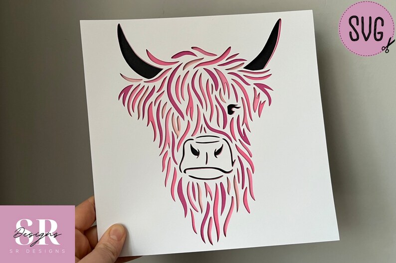 Puede incluir: Un dise&ntilde;o de corte de papel rosa y negro de la cabeza de una vaca de las tierras altas. El dise&ntilde;o es intrincado y detallado, con el pelo de la vaca representado por papel en capas.