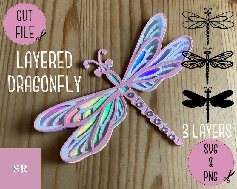 May include: A layered dragonfly craft project with three layers. The dragonfly is pink and iridescent. The image includes the text "CUT FILE", "LAYERED DRAGONFLY", "3 LAYERS", "SVG & PNG".