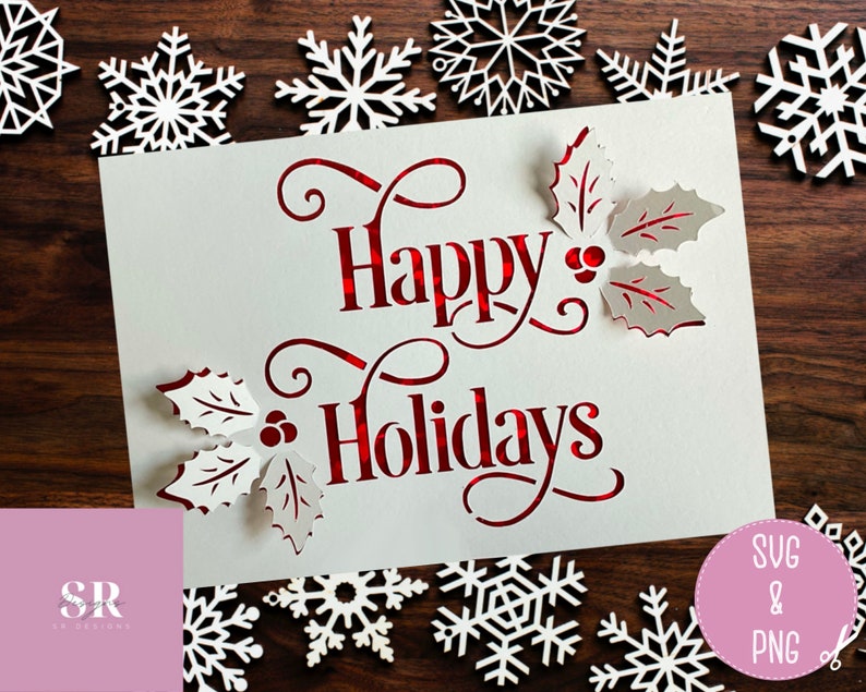 Puede incluir: Una tarjeta blanca con letras rojas que dice "Happy Holidays" con hojas de acebo y bayas recortadas alrededor del texto. La tarjeta est&aacute; rodeada de copos de nieve blancos sobre un fondo de madera.