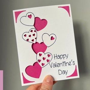 May include: A white card with a pink and white heart design. The card says "Happy Valentine's Day".