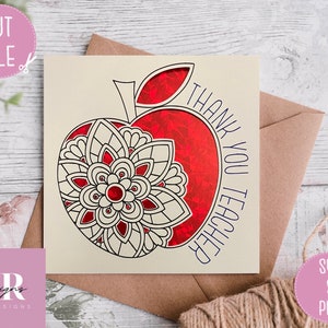 May include: A cream-coloured card with a red apple design and the words "THANK YOU TEACHER" in blue. The apple features a floral mandala design. The card is paired with a brown envelope and a twine string.