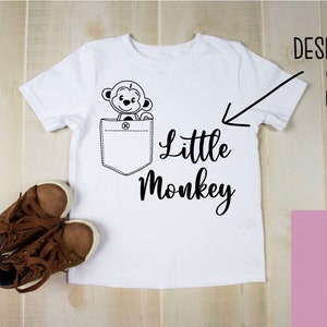 May include: White t-shirt with a black and white cartoon monkey in the pocket and the text "Little Monkey" below the pocket.