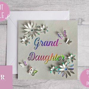 May include: A white card with a rainbow-colored text that says "Grand-Daughter" surrounded by cut-out flowers and butterflies.