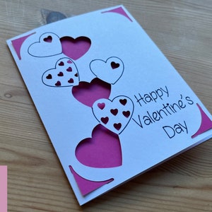 May include: A white card with a pink heart design and the text "Happy Valentine's Day".