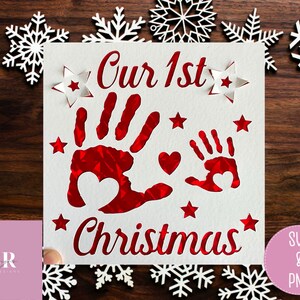 May include: A white card with red lettering that says "Our 1st Christmas". The card has two red handprints with hearts inside them and stars around the edges.
