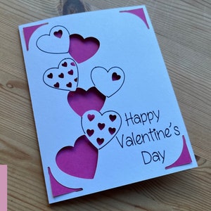 May include: A white card with a pink and white heart design. The card says "Happy Valentine's Day".