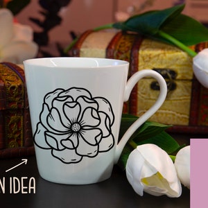 May include: White ceramic mug with a black outline of a flower design. The mug is sitting on a table with a wooden box and white tulips in the background. The text "DESIGN IDEA" is visible in the lower left corner of the image.