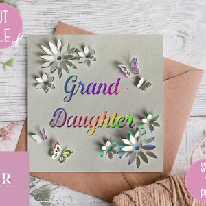 May include: A card with the words "Grand-Daughter" in rainbow colors and a floral design with butterflies. The card is on a wooden surface with a brown envelope and a pink square with the letters "SR" in white.