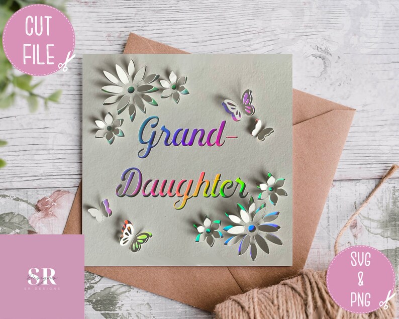 May include: A card with the words "Grand-Daughter" in rainbow colors and a floral design with butterflies. The card is on a wooden surface with a brown envelope and a pink square with the letters "SR" in white.