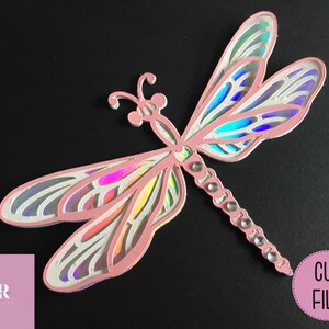 May include: A pink iridescent dragonfly cut file for crafting. The dragonfly has intricate details and a delicate design.