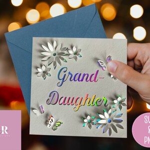 May include: A white card with the words "Grand-Daughter" in rainbow colors. The card has a cut-out design of flowers and butterflies.