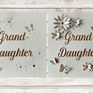 May include: Two white cards with the words "Grand-Daughter" cut out in brown paper. The cards are decorated with white paper flowers and butterflies.