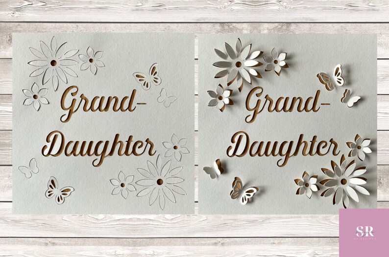 May include: Two white cards with the words "Grand-Daughter" cut out in brown paper. The cards are decorated with white paper flowers and butterflies.