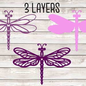 May include: Three layered purple and pink dragonfly cutouts on a white wood background. The text "3 LAYERS" is at the top of the image.