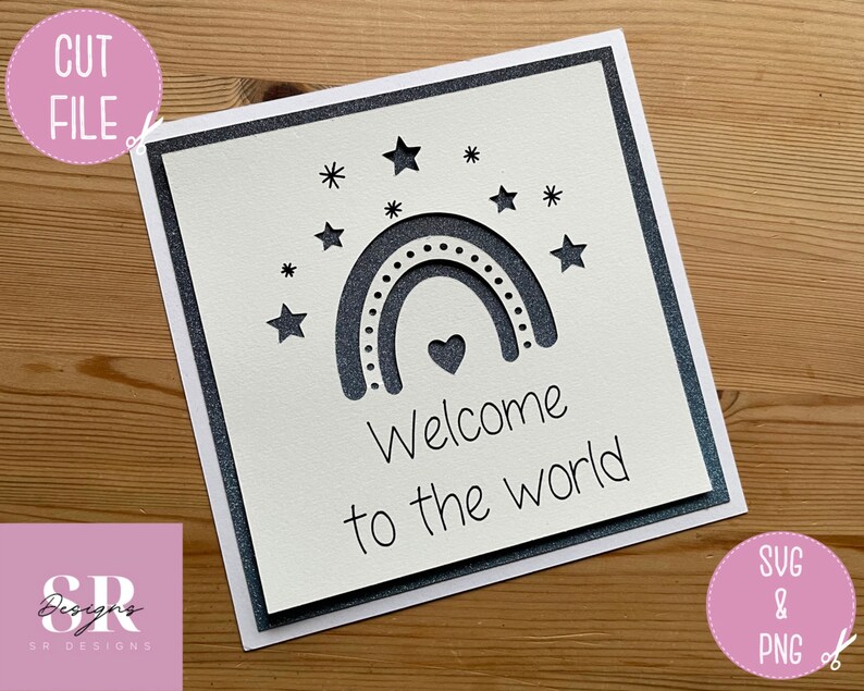 May include: A white card with a gray border and a cut-out design of a rainbow with stars and a heart. The text "Welcome to the world" is written below the rainbow.