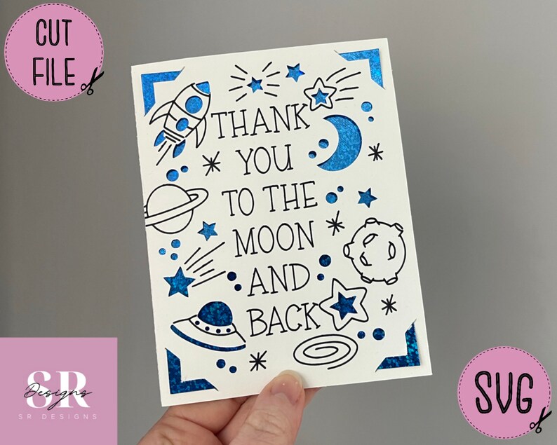 Op de afbeelding: Een witte kaart met een blauwe glitterrand en zwarte tekst die "Bedankt tot aan de maan en terug" luidt. De kaart is versierd met sterren, een raket, een planeet, een maan en een UFO.