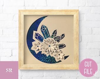May include: A digital cut file design featuring a crescent moon with a glittery blue and green texture. The moon is adorned with white paper flowers and crystal shapes.