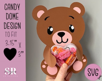May include: A brown teddy bear holding a clear heart-shaped container filled with candy. The container is 3.15 inches by 3 inches. The text "CANDY DOME DESIGN TO FIT 3.15" X 3"" is visible on the left side of the image.