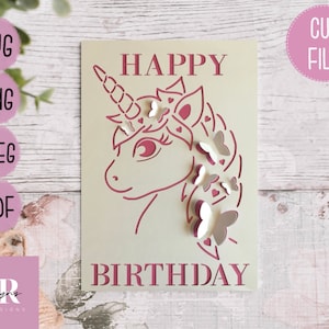 May include: A pink and white cut file design for a birthday card featuring a unicorn with a horn and a mane of butterflies. The text "Happy Birthday" is written below the unicorn.
