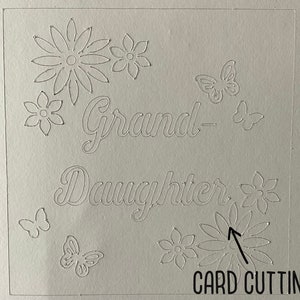 May include: A white card with the words "Grand-Daughter" cut out. The card is decorated with cut-out flowers and butterflies.