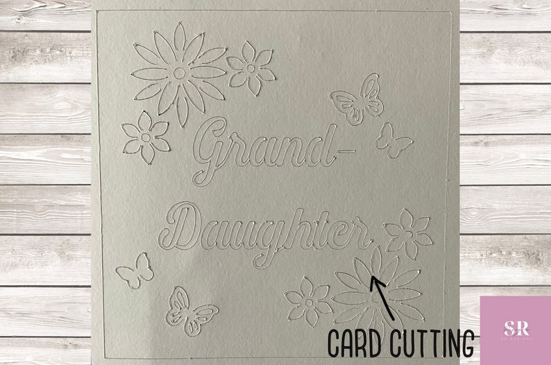 May include: A white card with the words "Grand-Daughter" cut out. The card is decorated with cut-out flowers and butterflies.