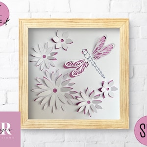 May include: A framed paper craft featuring a pink and white dragonfly with glitter accents surrounded by white paper flowers.