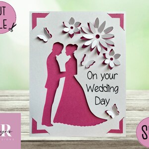 May include: A white and magenta wedding card with a cut-out design. The card features a silhouette of a bride and groom, flowers, and butterflies. Text on the card reads "On your Wedding Day". The card is a cut file.