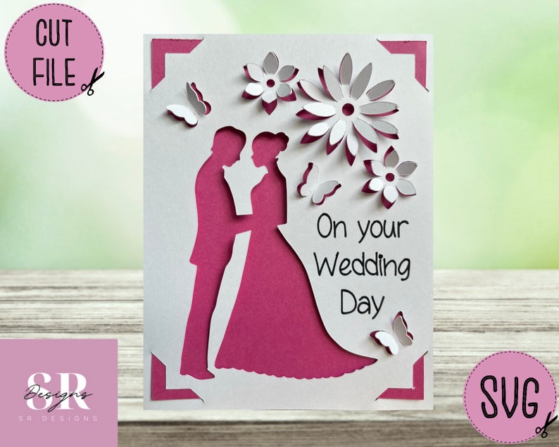 May include: A white and magenta wedding card with a cut-out design. The card features a silhouette of a bride and groom, flowers, and butterflies. Text on the card reads "On your Wedding Day". The card is a cut file.