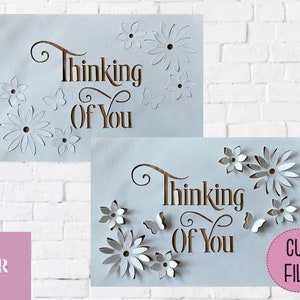 May include: Two white cards with the text "Thinking of You" in brown script. The cards have intricate cut-out designs of flowers and butterflies.
