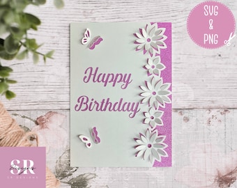 Può includere: Un biglietto bianco con uno sfondo di glitter viola e il testo "Happy Birthday" in corsivo viola. Il biglietto è decorato con ritagli di carta bianca a forma di farfalle e fiori.
