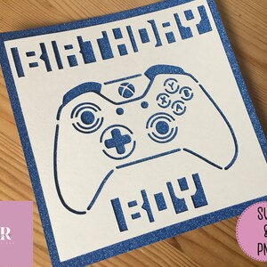 Könnte beinhalten: Eine weiße Karte mit einem blauen Rand und einem blauen Videospiel-Controller-Design. Der Text "Happy Birthday" ist in Blau auf der Karte geschrieben.