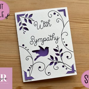 May include: A white card with a purple border and a black design of a bird and vines. The text "With Sympathy" is written in black cursive.