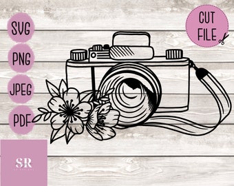 May include: A black and white line drawing of a vintage camera with a floral design. The camera has a lens, a strap, and a body with a film rewind knob. The floral design is made up of two flowers with five petals each.