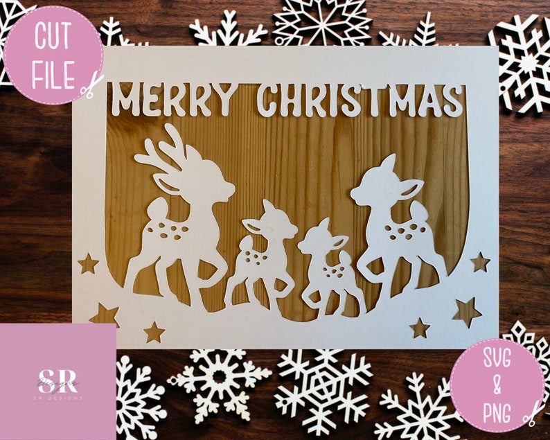 May include: White paper cut-out design featuring a family of deer with the words "Merry Christmas" at the top. The design is set against a woodgrain background.