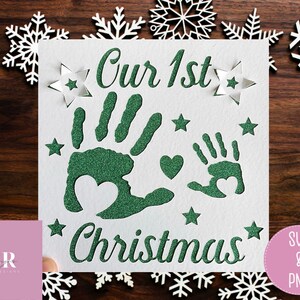 May include: A white card with green glitter handprints and the text "Our 1st Christmas" surrounded by white stars.