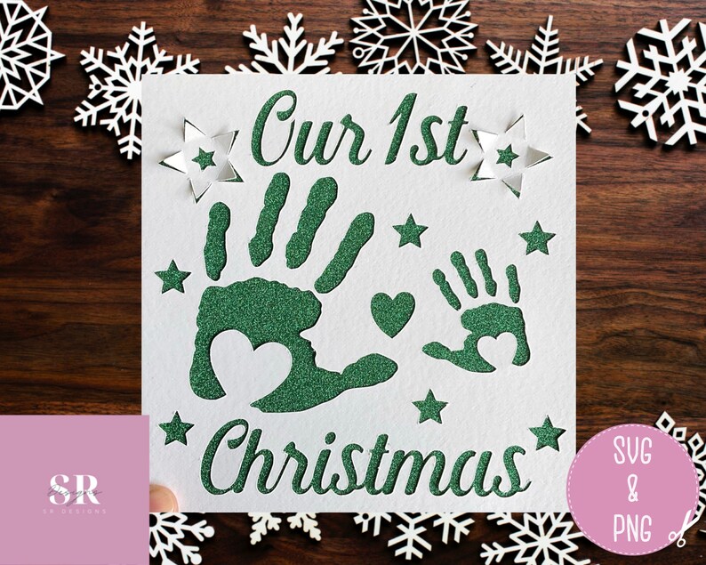 May include: A white card with green glitter handprints and the text "Our 1st Christmas" surrounded by white stars.