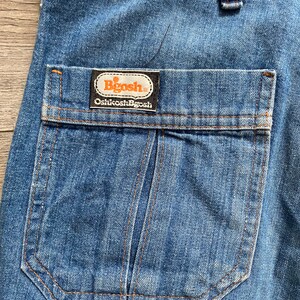 May include: Close-up of a blue denim pocket with a brown label that reads "Bigosh Oshkosh B'Gosh".