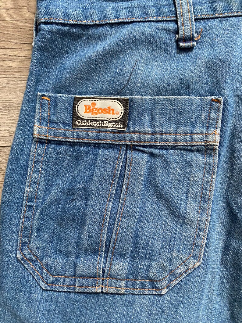 May include: Close-up of a blue denim pocket with a brown label that reads "Bigosh Oshkosh B'Gosh".