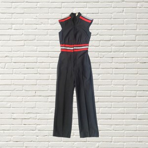 K&ouml;nnte beinhalten: Schwarzer &auml;rmelloser Jumpsuit mit einem roten und wei&szlig;en Streifen-Detail um die Taille.